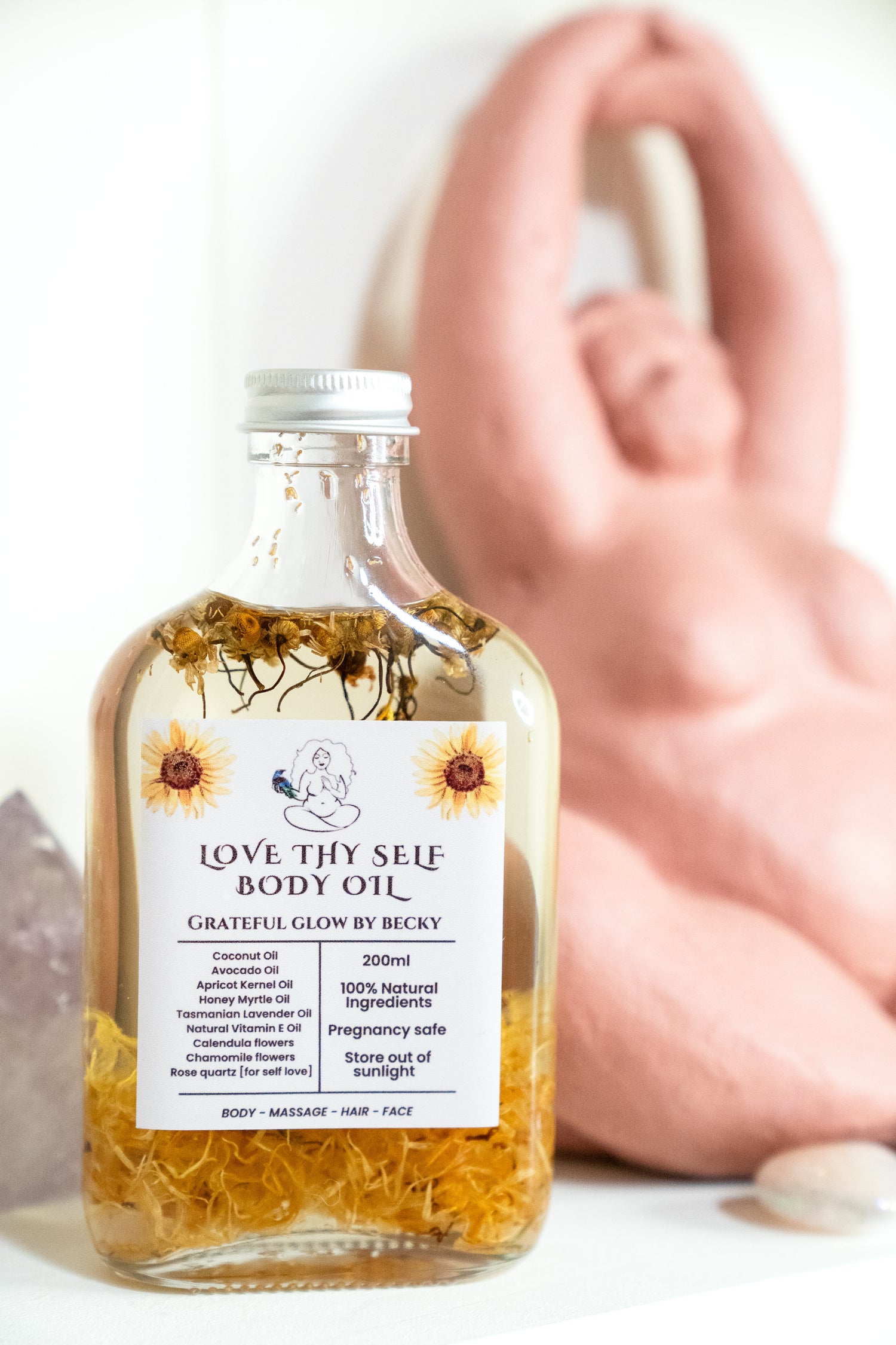 Bottle of 'Love Thy Self' body oil with a label, placed on a surface with a blurred background.