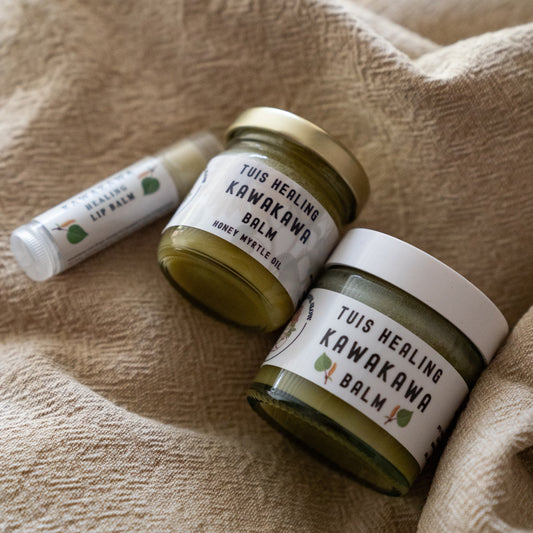 Two jars of Tuis Healing Kawakawa Balm and one lip balm tube resting on a textured beige linen cloth.