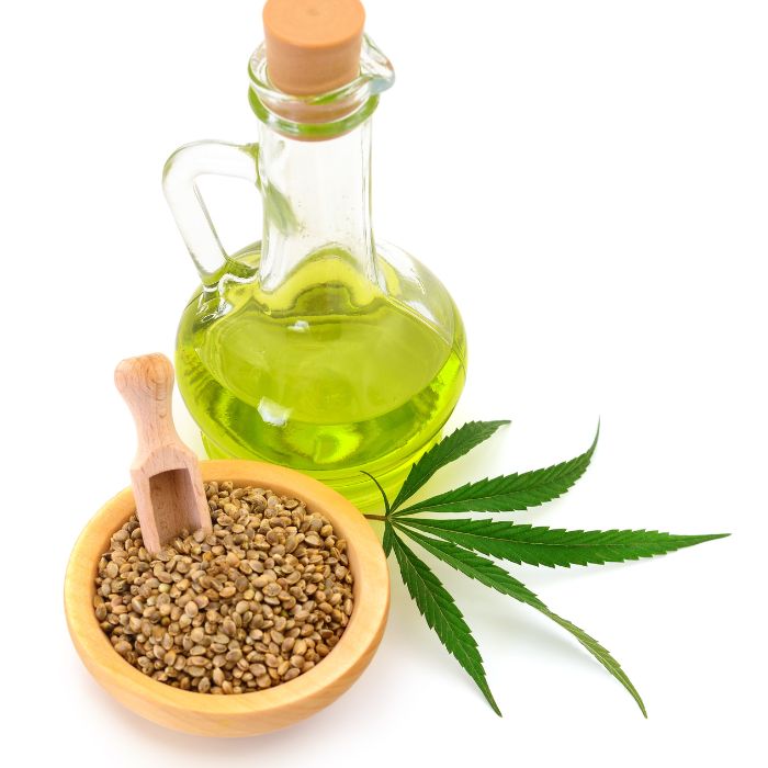 Glass bottle of green liquid, wooden bowl with seeds, and cannabis leaf on a white background