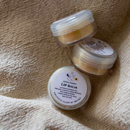 Three small round jars of lip balm arranged on a textured beige fabric background.